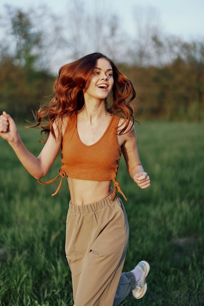 A happy athletic woman is jogging and smiling in nature in the park summer sunset light