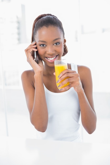 オレンジジュースを持っている間に電話をかける幸せな運動女性