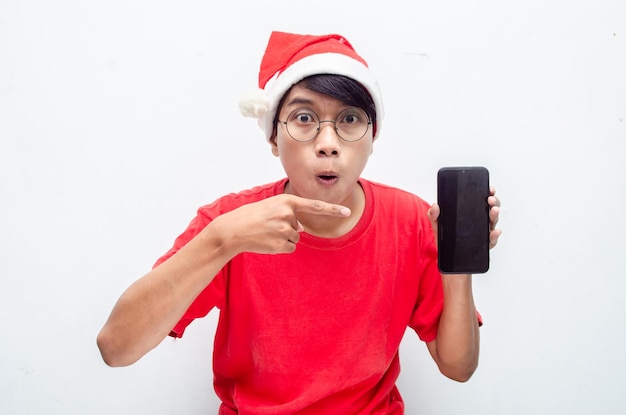 赤いクリスマス テーマの服を着た幸せな魅力的なアジア人男性は、携帯電話を持っている間、喜んでショックを受けました。