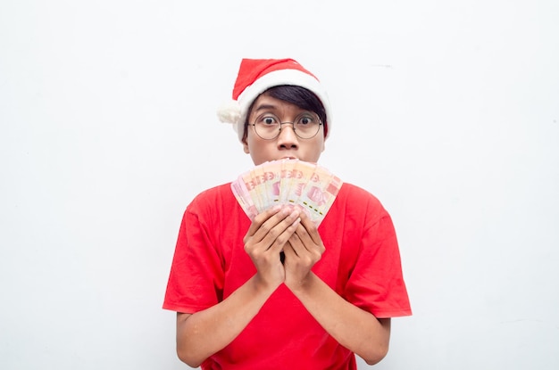 happy attractive Asian man in red Christmas theme clothes shocked happily while holding rupiah money