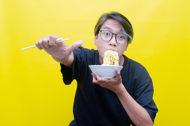 Happy attractive asian man with peek a boo hair eats noodles hungrily on bowl with chopstick