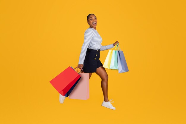 Happy attractive black woman with shopping bags jumping on yellow