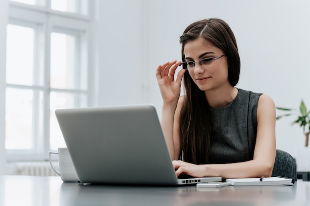 Happy attractive business woman in glasses working with laptop in office