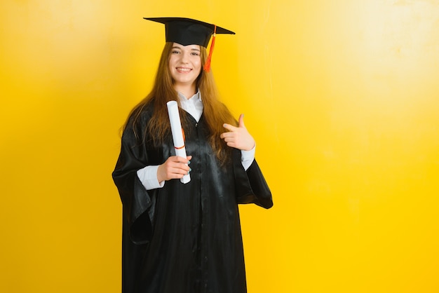 Felice attraente laureato in abito da maestro, con un diploma su una parete gialla.