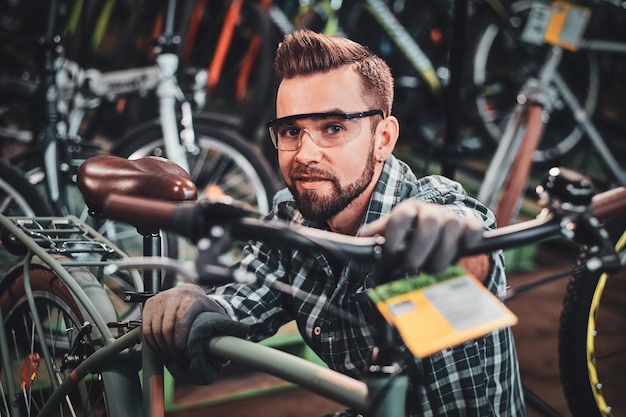 Foto felice uomo attraente in occhiali protettivi e camicia sta controllando la catena di biciclette per il cliente.