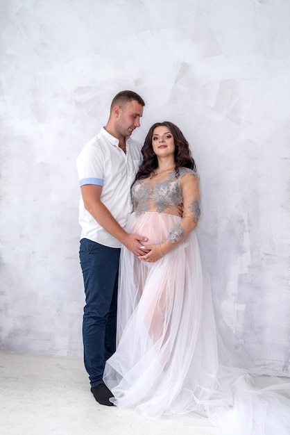 Happy and attractive pregnant couple posing in studio. Husband tender hugging  his wife