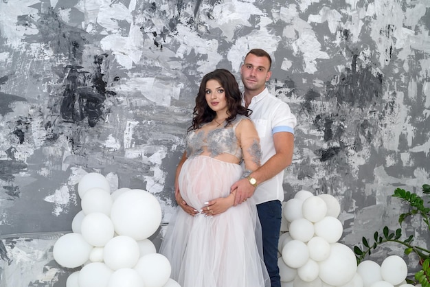 Happy and attractive pregnant couple posing in studio. Husband tender hugging  his wife