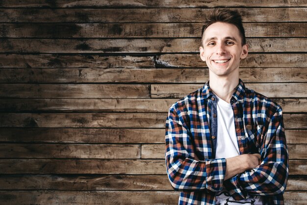 Happy attractive young man in plaid shirt standing and smiling over wooden background