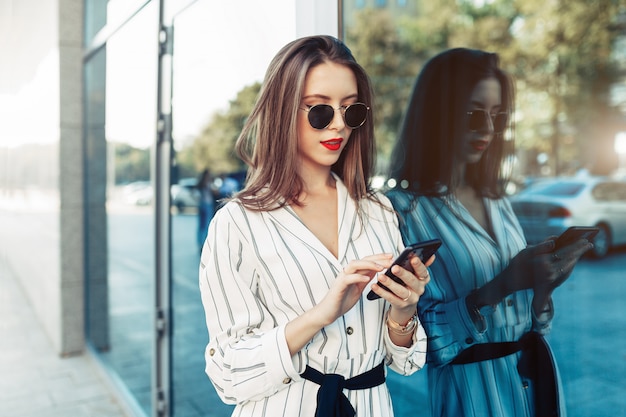 Felice attraente giovane donna in occhiali da sole guardando lo schermo dello smartphone