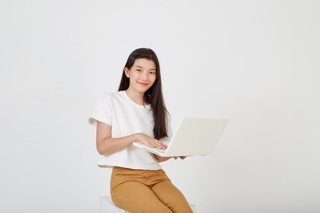 Happy attractive young woman with laptop computer sitting cross legged and looking at empty space on white studio background