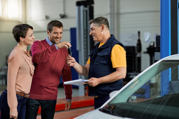 Happy auto repairman receiving car key from his customers in a workshop