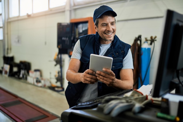 Happy auto repairman using desktop PC and digital tablet while working in a workshop