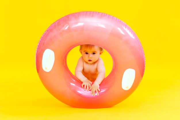 Happy baby of 10 months with a swimming circle sits on a yellow background, studio photo of the baby in a swimming circle