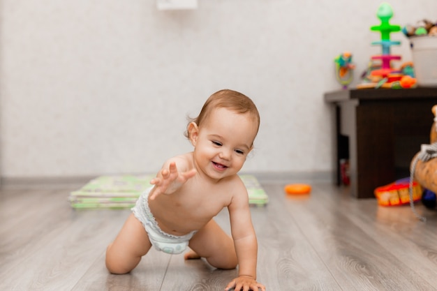 Il bambino felice di 11 mesi striscia sul pavimento e ride. il bambino è seduto sul pavimento.