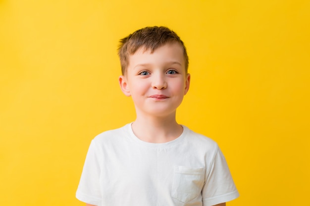 黄色の背景に白いTシャツで7歳の幸せな男の子