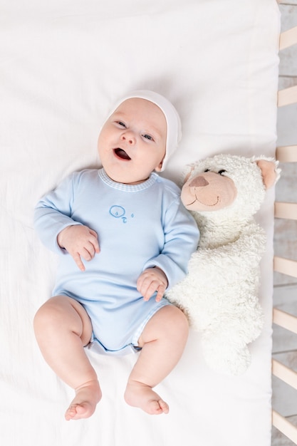 Happy baby boy in crib with teddy bear toy, children and birth concept