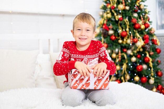 Счастливый малыш радуется подаркам, малыши дома на рождественские каникулы. новогодние каникулы. малыш находится в празднично украшенной комнате с елкой. портрет ребенка