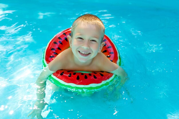 happy baby boy learns to swim in a blue pool with a bright red inflatable circle