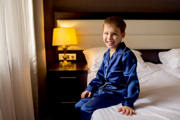 Happy baby boy in pajamas sitting on the bed