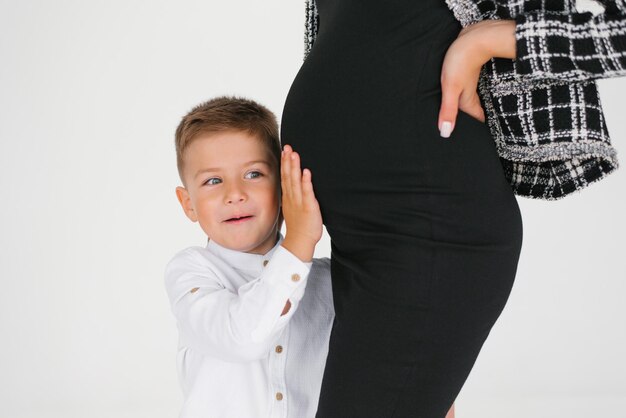 Фото Счастливый мальчик слушает и держит руки на животе своей беременной матери, ожидающей.