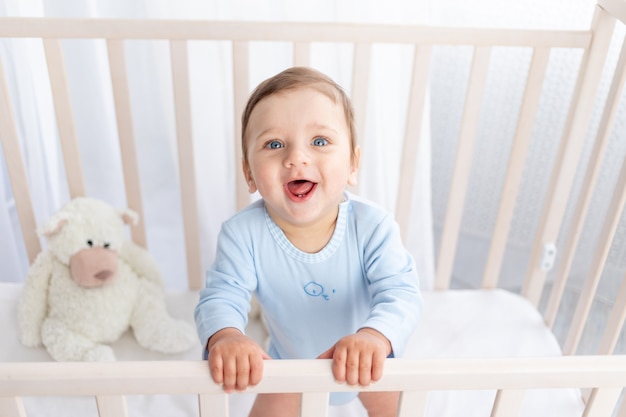 Happy baby boy staat in de wieg in de kinderkamer en lacht of lacht