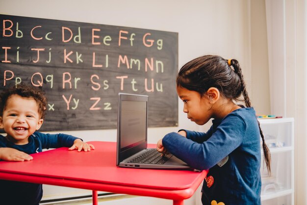 happy baby boy standing by table while sister studying over laptop