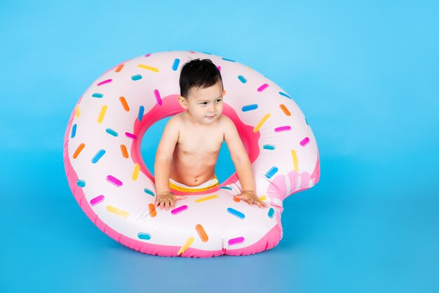 Happy baby boy in swimsuit with swimming ring donut on a colored blue wall