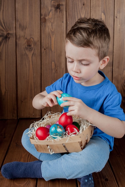 Счастливый малыш с корзиной пасхальных яиц на деревянном фоне