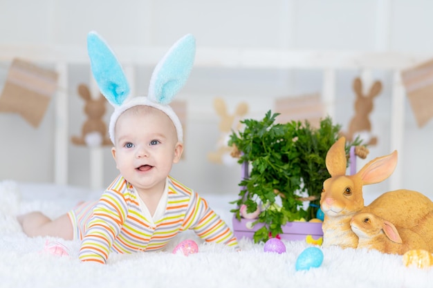 머리에 토끼 귀를 가진 행복한 아기 부활절 달걀을 안고 침대에 토끼를 안고 누워 있는 행복한 아기 귀엽고 웃긴 웃는 아기 부활절의 개념