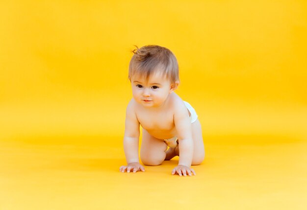 Happy baby crawling isolated on a yellow background. baby in diaper creeps