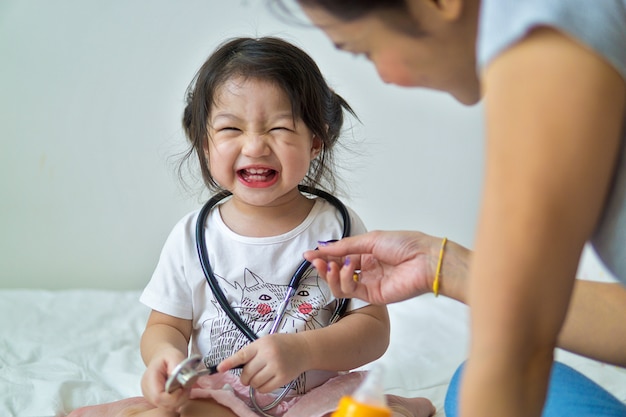 Happy baby girl having fun with mother in bed.