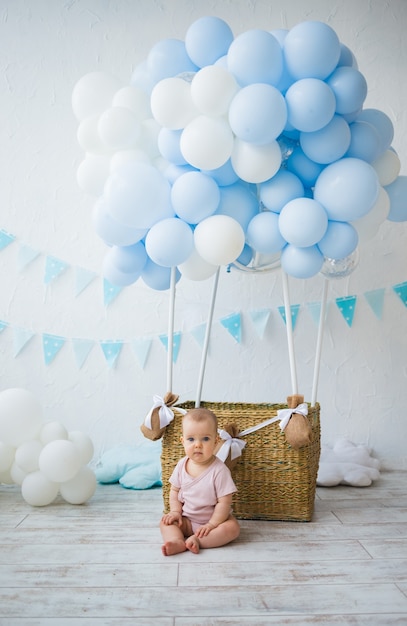 Happy baby girl sitting near a wicker basket with balloons on a white background