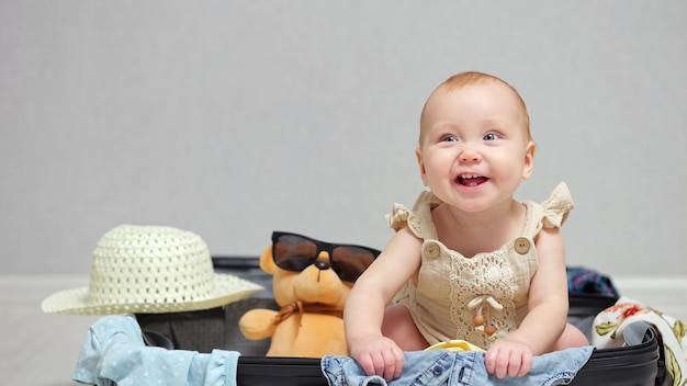 Happy baby girl sitting in suitcase smiles and laughs