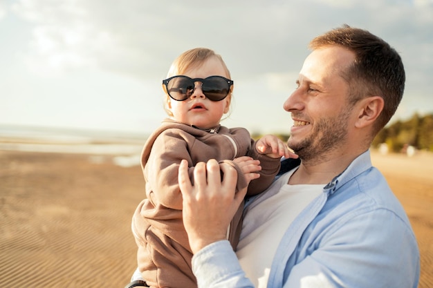 Happy baby girl in sunglasses playing with dad in nature