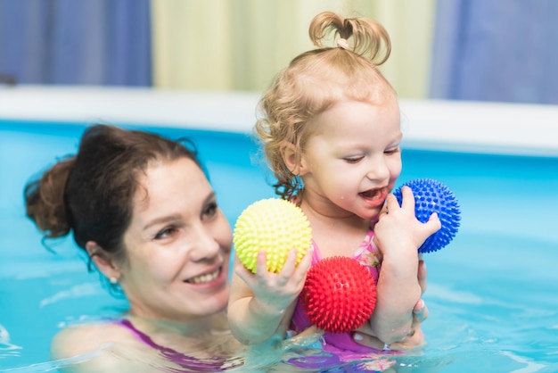 Happy baby girl swims in the pool with her mother