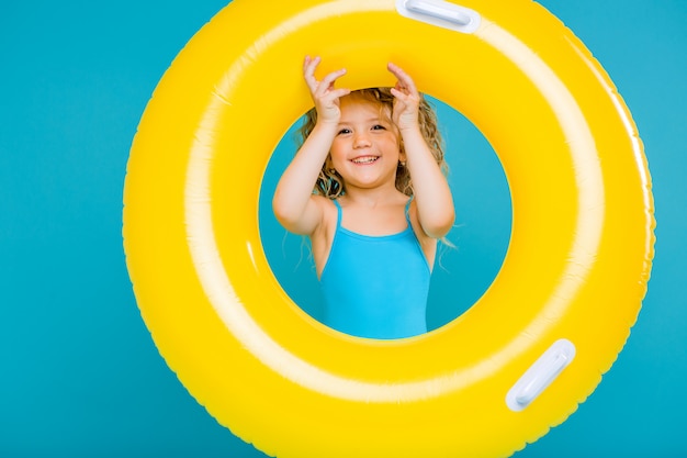 Happy baby girl in swimsuit with circle isolated on blue background