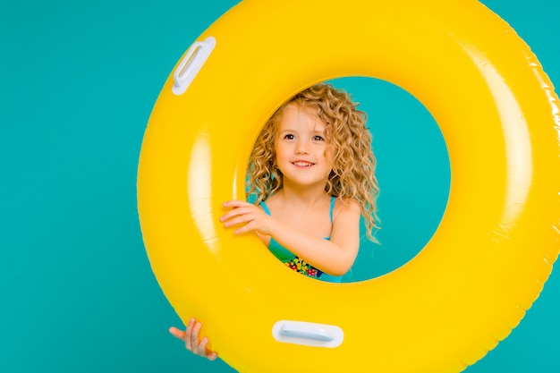 Happy baby girl in swimsuit with circle isolated on blue background