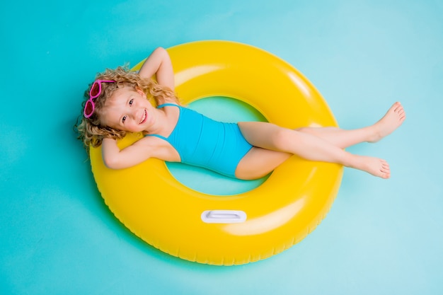 Happy baby girl in swimsuit with circle isolated on blue background