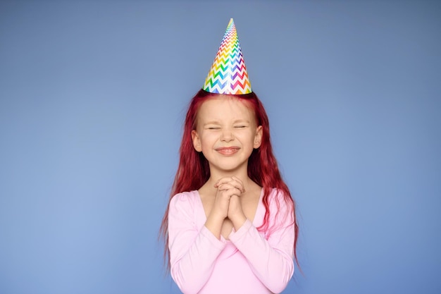 Photo happy baby girl wearing princess hat at birthday party over isolated lilac background.