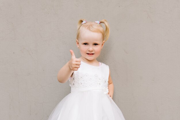 Happy baby girl in white dress on grey