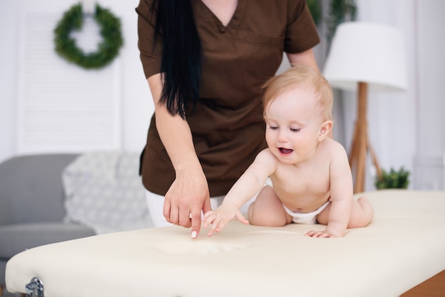 Happy baby having massage with professional female masseuse. Health care and medical concept. Kind and friendly children's doctor.