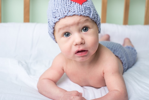 Happy baby is lying in a crib on a blanket in a knitted beanie with a heart