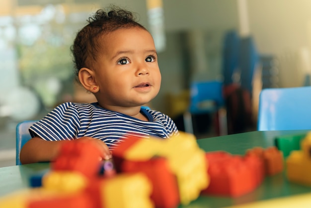 Happy baby playing with toy blocks in the kindergarten.