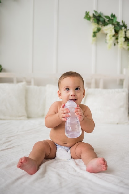 Felice bambino seduto in un pannolino sul letto con una bottiglia d'acqua