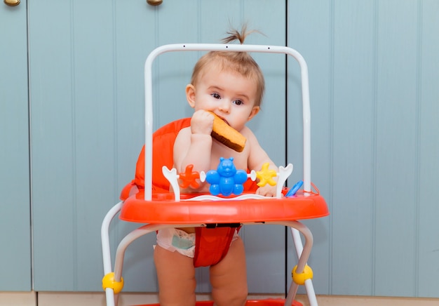 빨간 워커에 앉아서 크래커를 먹는 행복한 아기. 웃는 아기