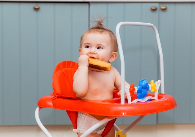 빨간 워커에 앉아서 크래커를 먹는 행복한 아기. 웃는 아기