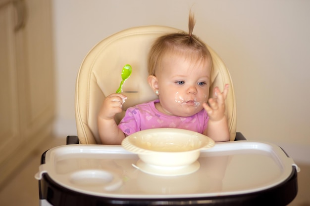 happy baby sitting at the table in the kitchen and eating with an appetite