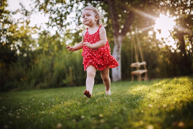 Счастливый ребенок, улыбающаяся маленькая девочка, бегущая в саду на закате на открытом воздухе босиком