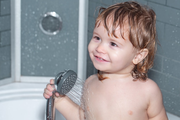 Happy baby taking a bath playing with foam bubbles. Child bathing under a shower. Infant washing and bathing. Kids care and hygiene.