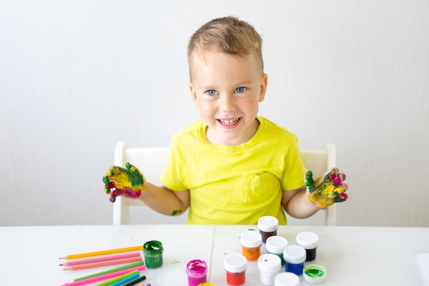 Счастливый ребенок ребенок рисует пальцами с яркими улыбками цветов смотрит в камеру